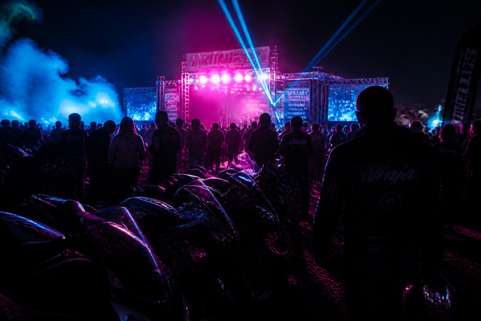 Riders and bikes lit by stage lights at a night moto festival